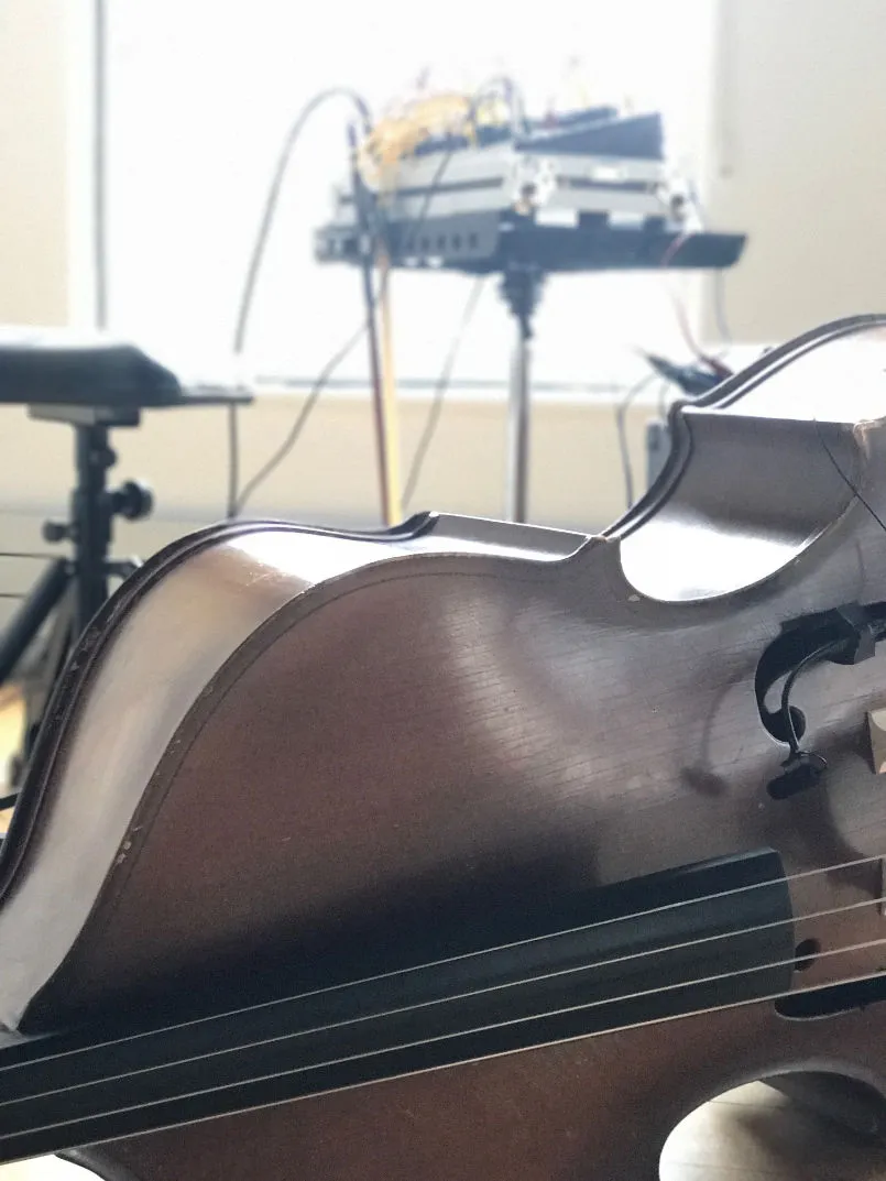 a double bass with a microphone attached. in the background a modular synth